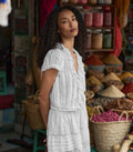 Woman in a white blouse standing in a market setting with various products and baskets.