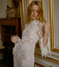 Woman in a white floral crochet dress holding a glass in an elegant room.