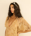 Woman wearing a gold lace dress with a plain background