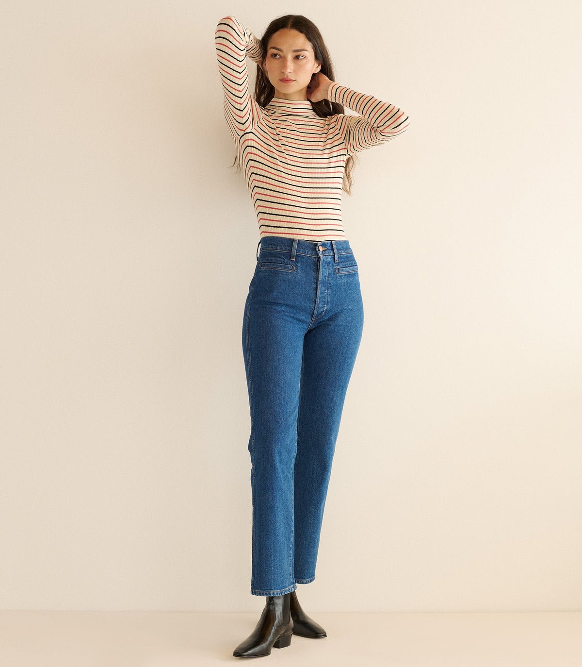 Woman wearing a striped sweater and blue jeans against a beige background