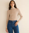 Woman wearing a striped long-sleeve top and blue jeans against a beige background