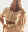 Woman wearing a white crochet top and skirt sitting in a softly lit room.